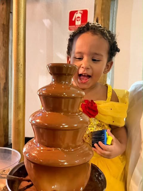 Menina diante da cascata de chocolate na festa de 3 anos